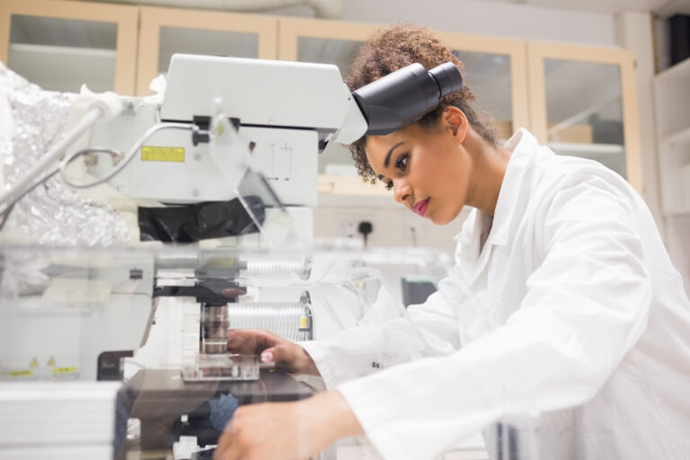 Pretty science student using microscope at the university